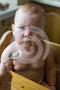 Serious baby sits on a chair and doesnÃ¢â¬â¢t want to eat with spoon